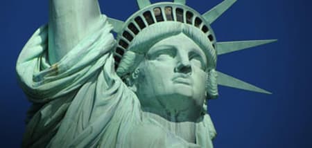Close-up of the Statue of Liberty's weathered copper face and crown against a blue sky.