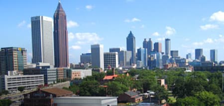 Atlanta's modern skyscrapers rise above a green tree line under a clear blue sky.