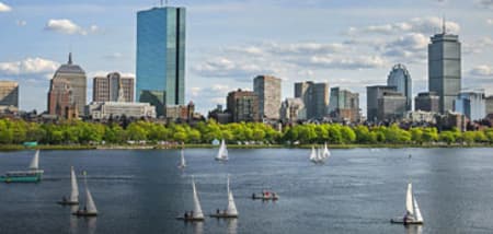 Boston's skyline with sailboats on the Charles River under a partly cloudy sky.