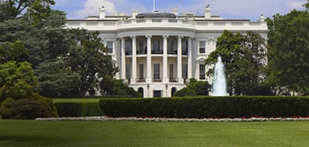 The White House with a fountain on a sunny day, surrounded by green trees.