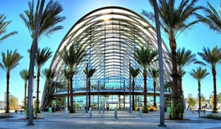 Modern building with a large arched glass roof and tall palm trees.