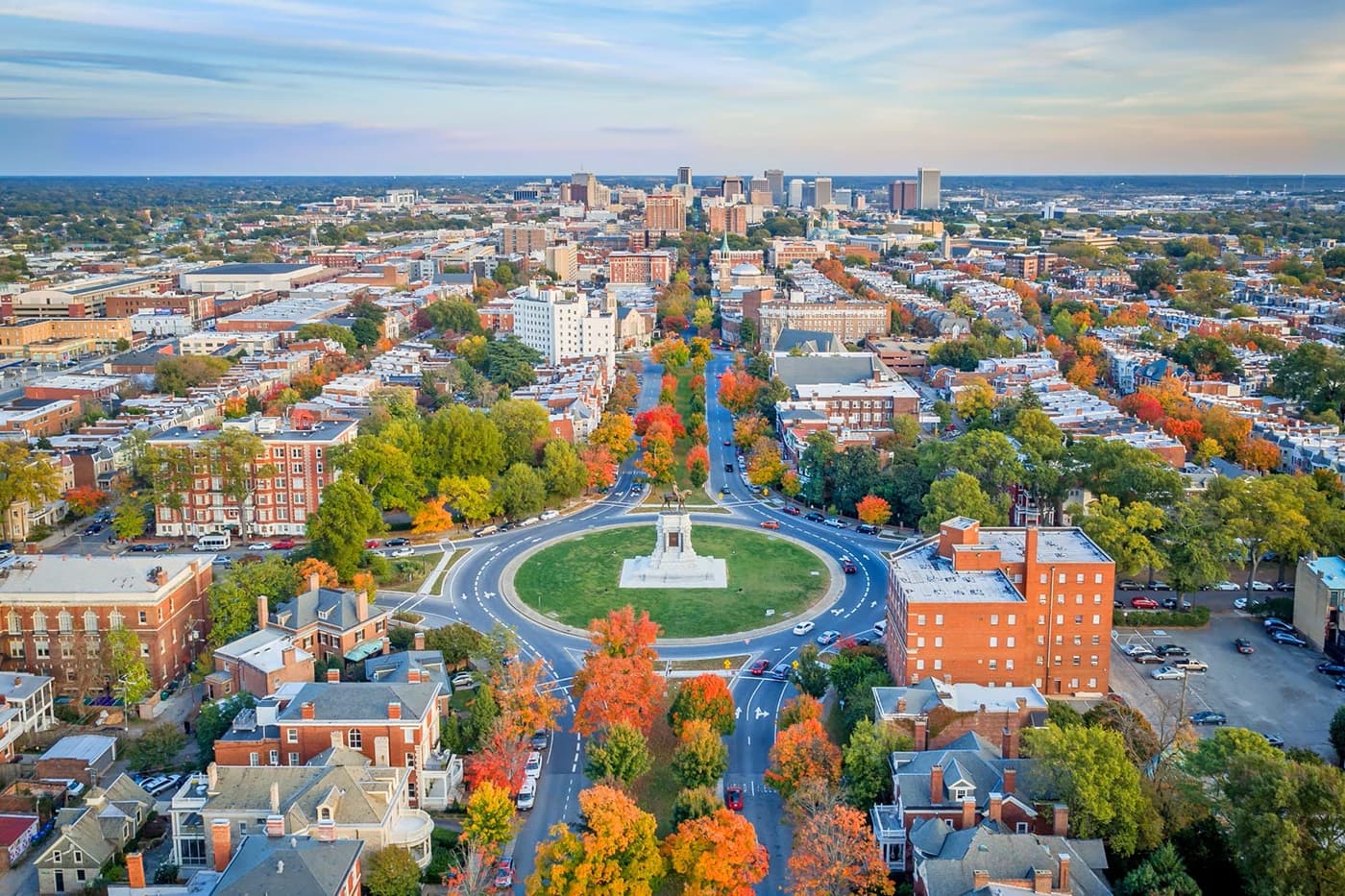 Aerial view of a city with a large circular monument in a roundabout, surrounded by colorful autumn trees.