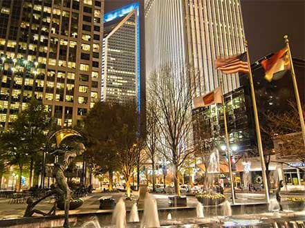 Charlotte city skyline at night with illuminated skyscrapers, flags, and a fountain.