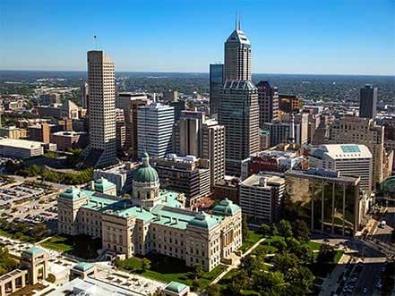 Aerial view of Indianapolis skyline featuring the Statehouse with a green dome and modern skyscrapers.