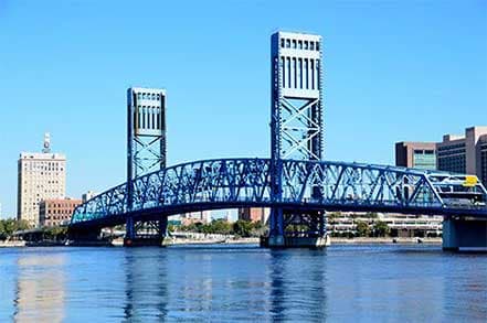 A large blue drawbridge spanning a river with city buildings in the background.