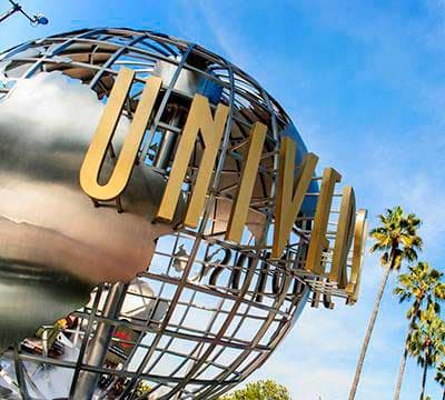 Large metallic Universal Studios globe with gold letters and palm trees against a blue sky.
