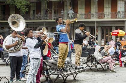 A brass band performs in a New Orleans square with people sitting on benches.