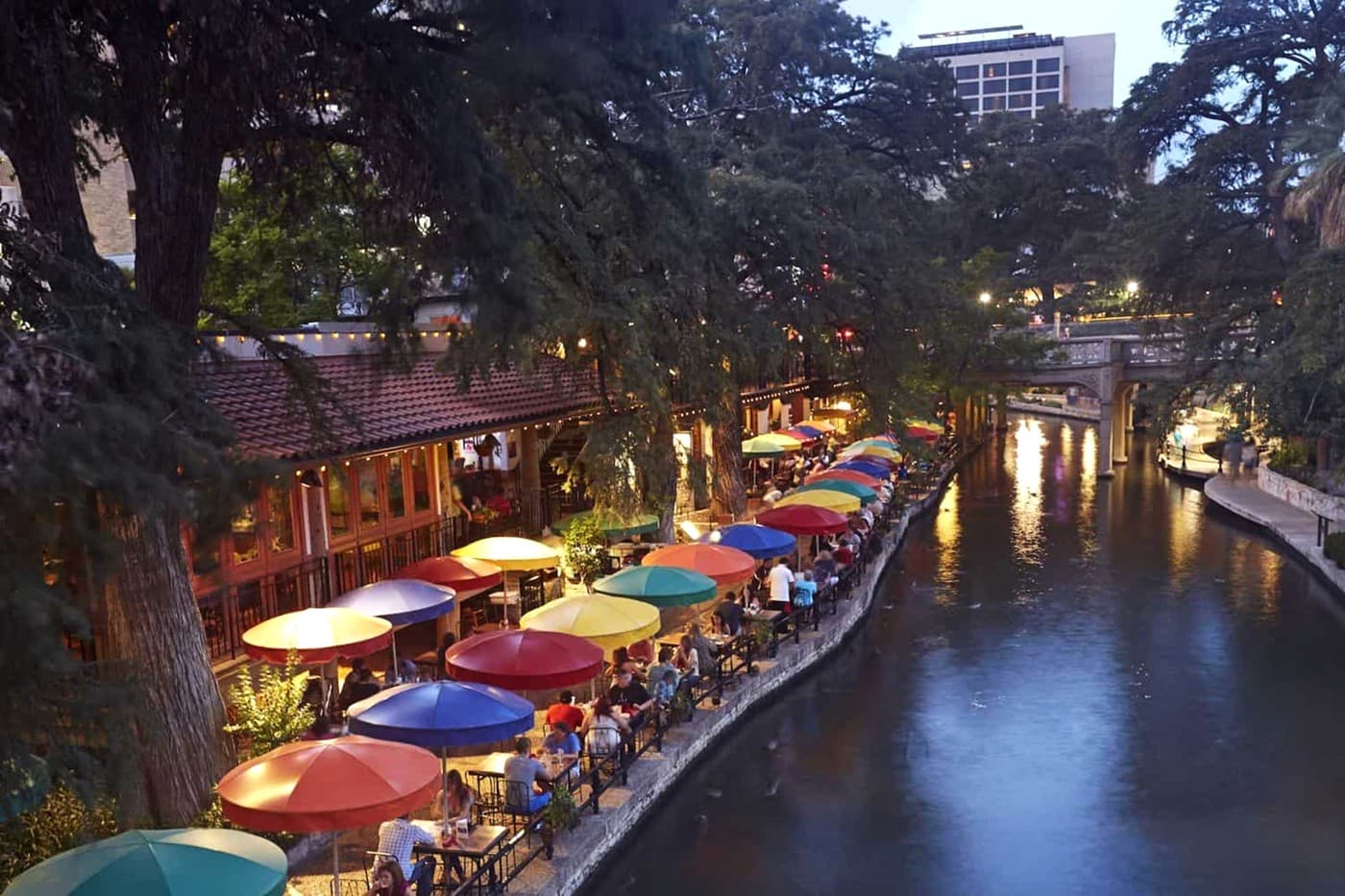 San Antonio Riverwalk at dusk, with colorful umbrellas shading outdoor dining areas.