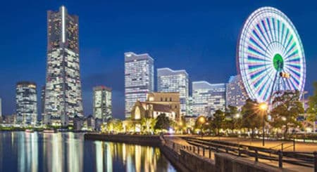 Illuminated Yokohama cityscape at night with a Ferris wheel reflected in water.