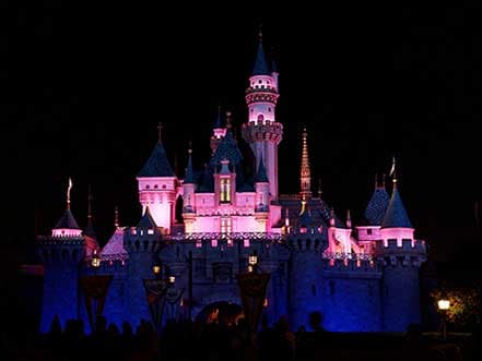Sleeping Beauty Castle at Disneyland illuminated with pink and blue lights at night.