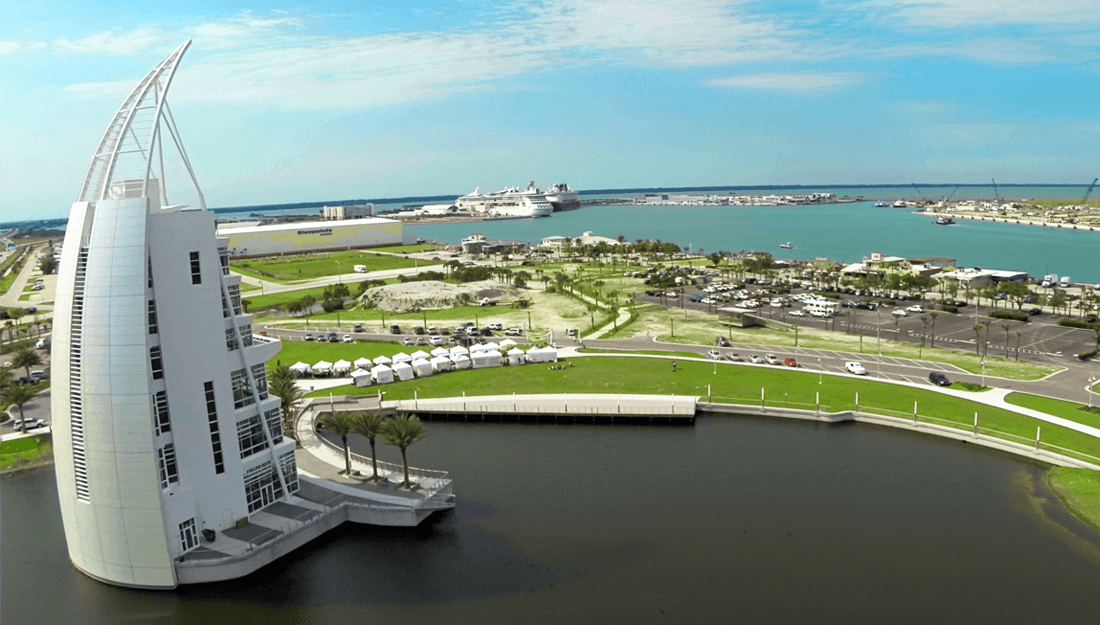 Modern white sail-shaped building overlooks a busy harbor with a large cruise ship.